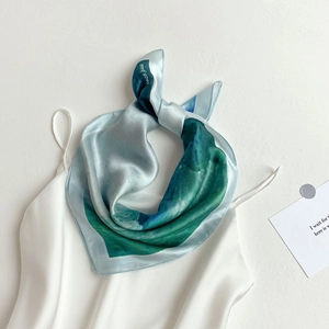 Close-up of silk square scarf featuring teal marble pattern on a white satin top