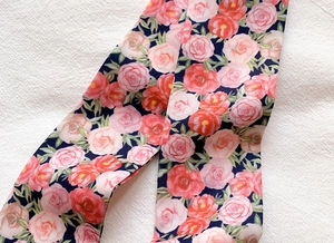 Detailed close-up of dark blue floral scarf with pink and orange roses on white fabric
