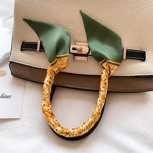 Detail of floral silk scarf wrapped on white leather handbag handle with gold lock