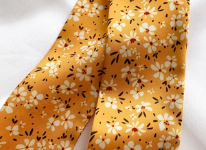 Close-up of a twill floral scarf with white flowers and orange fabric texture