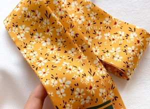 Detail of yellow floral silk scarf featuring daisy patterns and dark green stripe borders