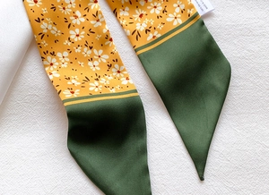 Detailed macro view of 100% silk twilly scarf with yellow floral pattern and stitching
