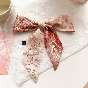 Gros plan d'un foulard en soie beige avec lettre A, motifs floraux et nœud décoratif chic