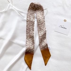 Detail of floral silk skinny scarf tied on a white dress showing elegant texture