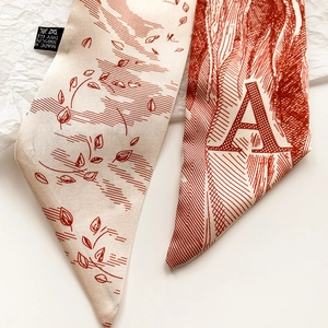 Détail d'une écharpe fine avec imprimé lettre A et motif de feuilles sur fond blanc
