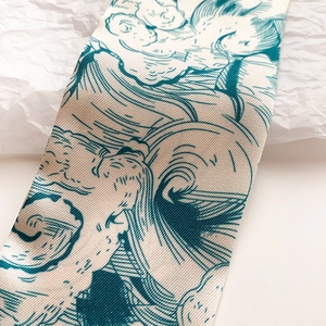 Détail macro d'un foulard en soie à motif de vagues turquoise sur fond blanc cassé