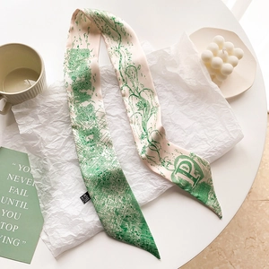 Détail d'un twilly en soie rose avec motif floral et lettre P sur une table blanche