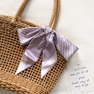 Detail of light purple striped silk scarf tied in a bow on a woven straw handbag