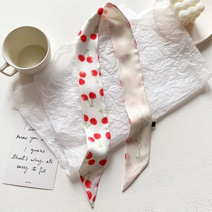 Dettaglio di un sottile foulard di seta crema con ciliegie rosse e scritta elegante