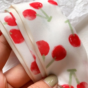 Dettaglio di uno scialle stretto in seta con vivaci ciliegie rosse su tessuto bianco