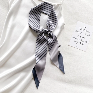 Detail of grey striped satin skinny scarf styled on a white silk dress neckline