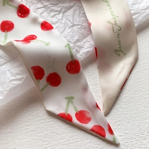 Dettaglio macro della sciarpa twilly con motivo a ciliegia su tessuto twill panna