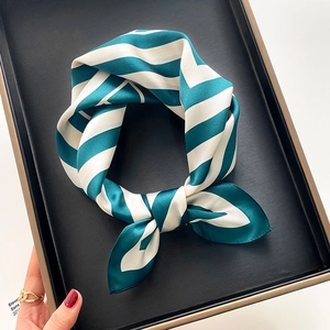 Classic teal and cream striped silk scarf tied in a bow on a black textured display tray