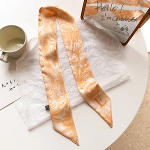 Détail d'un élégant foulard twilly en soie orange avec imprimé palmier pour cheveux
