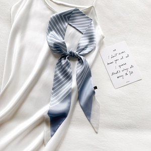 Elegant blue and white striped silk scarf tied on a white satin slip dress on linen background