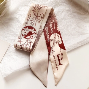 Détail d'un foulard étroit en soie avec motifs floraux et lettre F sur fond blanc