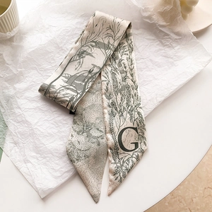 Détail d'un foulard étroit en soie avec motif oiseau et lettre G sur papier blanc