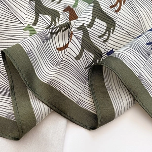 Detail of silk square scarf showing equestrian horse print and green stitched edges