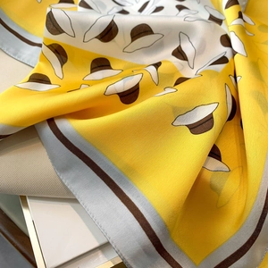 Close-up of yellow silk scarf with hat print showing soft fabric texture and fine stitching