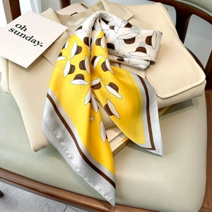 Detail of yellow silk scarf with hat pattern draped on beige vest showing smooth texture