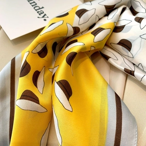 Close-up of yellow silk scarf featuring elegant hat patterns and brown stripes