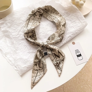 Détail d'un foulard étroit beige avec imprimé carte vintage et lettre M sur fond crème
