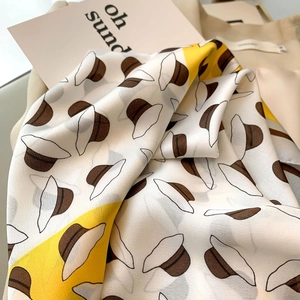 Detailed view of yellow floral silk scarf fabric with elegant hat print and soft luster