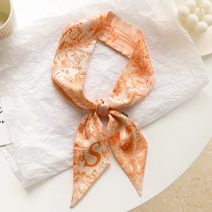 Détail d'un foulard en soie twilly avec lettre S orange et motif tropical chic