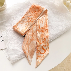 Détail d'un foulard en soie orange avec lettre S et imprimé léopard sur papier blanc