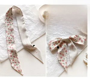 Detail of floral silk twilly scarf with pink buds and elegant cursive text accents