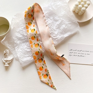 Detail view of pink silk scarf with orange fruit patterns and text on white artistic paper
