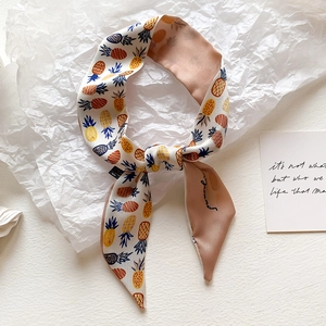 Detail of colorful pineapple print on a cream satin narrow scarf tied in a stylish knot