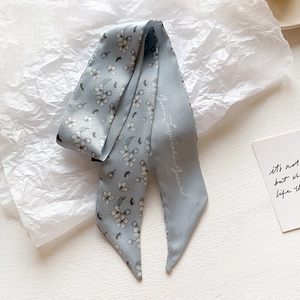 Detailed shot of a light blue satin silk Twilly scarf with floral prints on a white base
