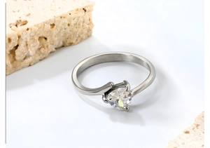 Gros plan d'une bague en argent avec zircon en forme de cœur et anneau poli sur pierres blanches