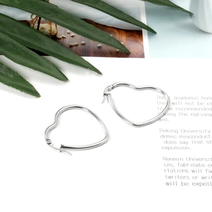 Macro shot of silver heart shaped hoop earrings on aesthetic paper with green leaves