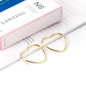 Detail shot of gold heart-shaped hoop earrings on a light aesthetic background