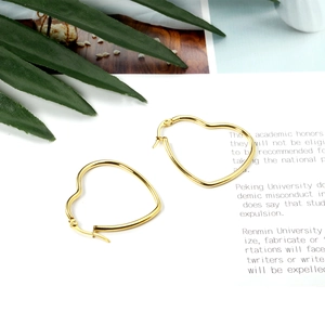 Detailed close-up of polished gold heart hoop earrings on a nature-inspired background