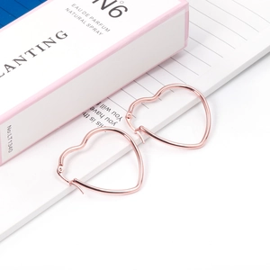 Detail of rose gold heart-shaped hoop earrings on striped paper with a pink gift box