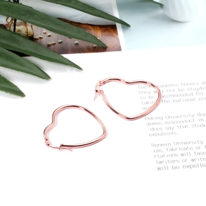 Polished rose gold heart-shaped hoop earrings displayed on a book with green leaves
