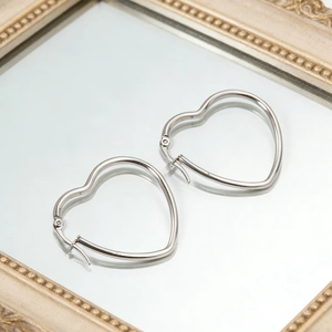 Minimalist silver heart hoop earrings on a vintage mirror with elegant reflections