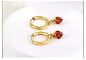 Détail de boucles d'oreilles cœur dorées avec zircons rouges sur support cylindrique
