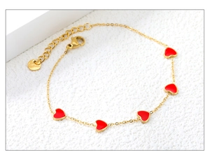 Dettaglio macro del bracciale in acciaio dorato con cinque cuori in smalto rosso
