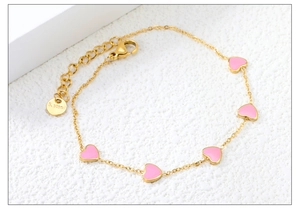 Dettaglio di ciondoli a cuore in smalto rosa su bracciale in acciaio dorato