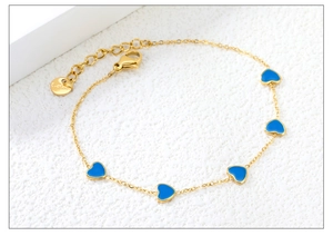 Dettaglio macro del bracciale in acciaio dorato con cinque ciondoli cuore in smalto blu