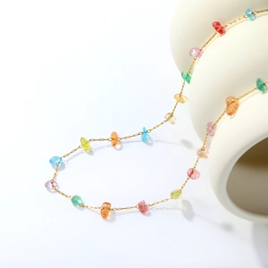 Detail of colorful irregular glass beads on a gold chain draped over a ceramic vase