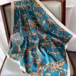 Détail d'un carré de soie avec motif de chaîne équestre dorée sur tissu sarcelle foncé