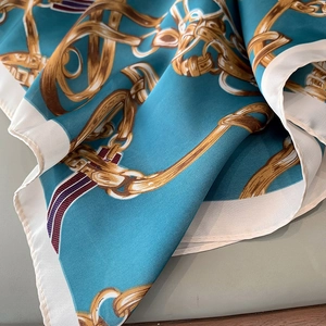 Gros plan d'un foulard carré en soie bleue avec motifs de chaînes dorées et ceintures