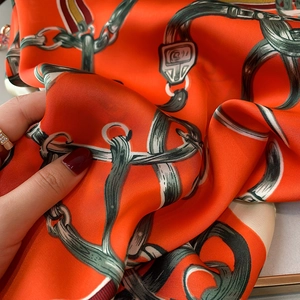 Gros plan sur un foulard en soie orange vif avec motifs équestres de ceintures et chaînes