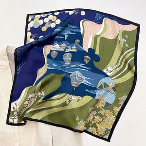 Detailed close-up of patterned silk scarf featuring balloons and mountains over a blazer