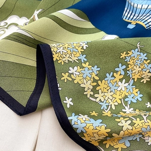 Detailed close-up of premium silk scarf with green floral patterns and fine rolled edges